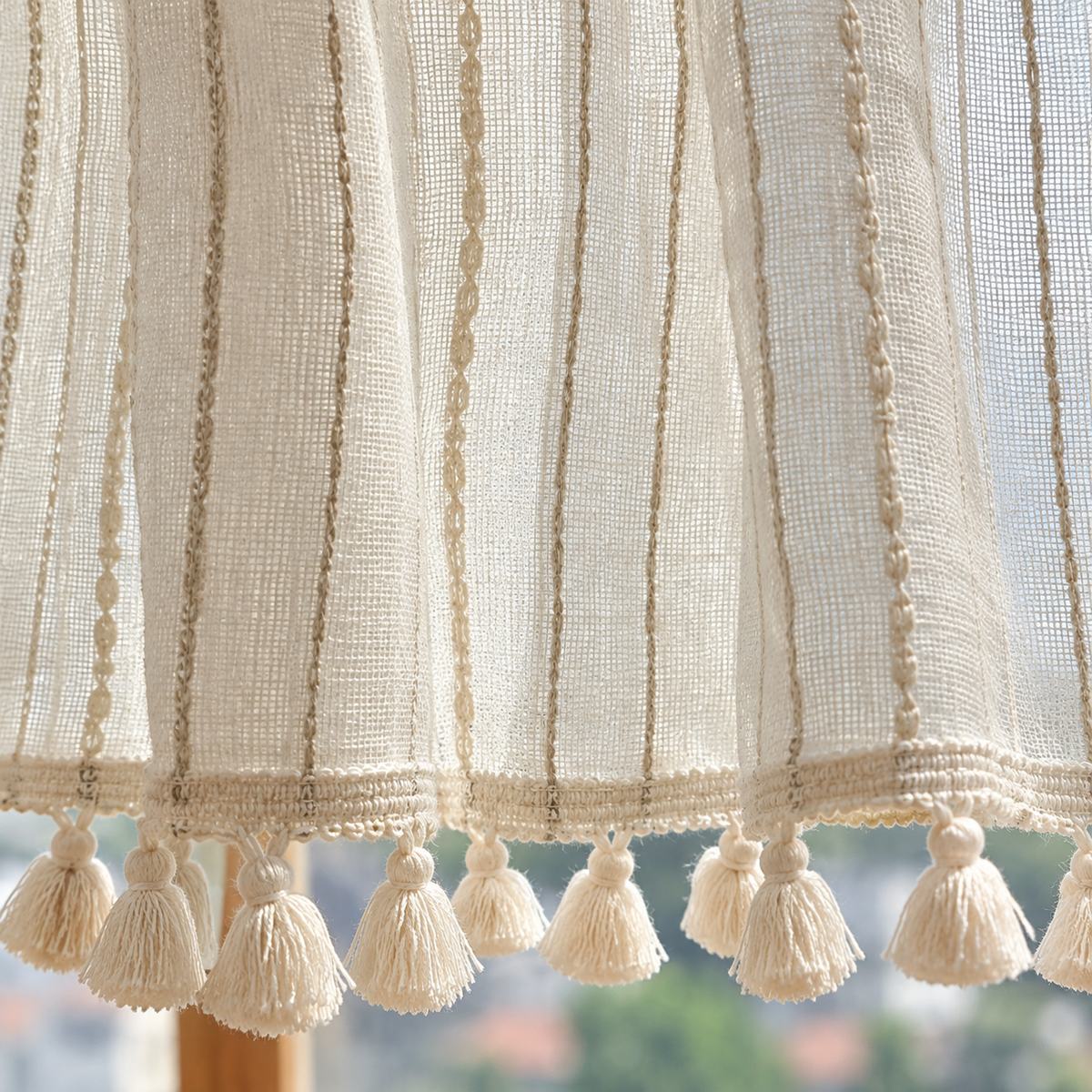 Brise-bise beige à rayures brodées, base tulle et pompons – détail de la matière