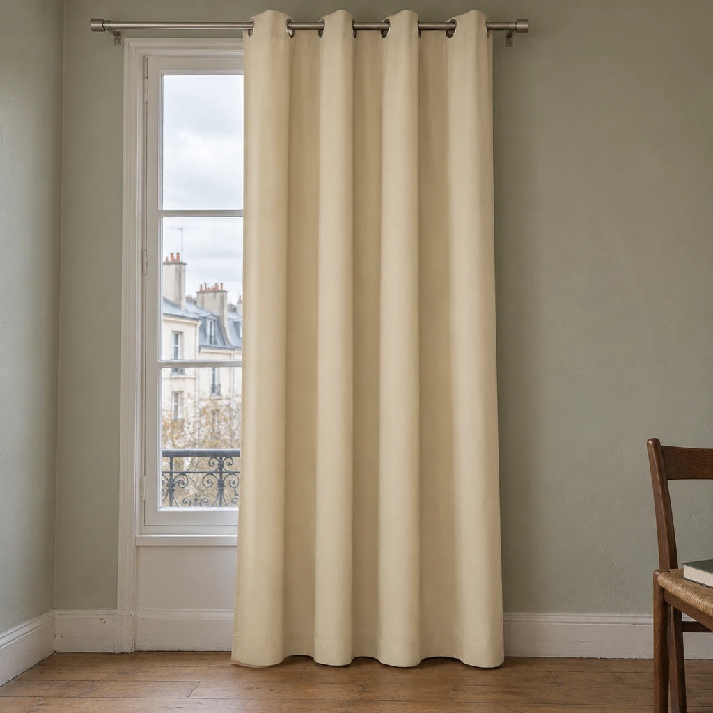 Rideau thermique uni beige à œillets, suspendu devant une fenêtre dans un intérieur aux murs gris vert.