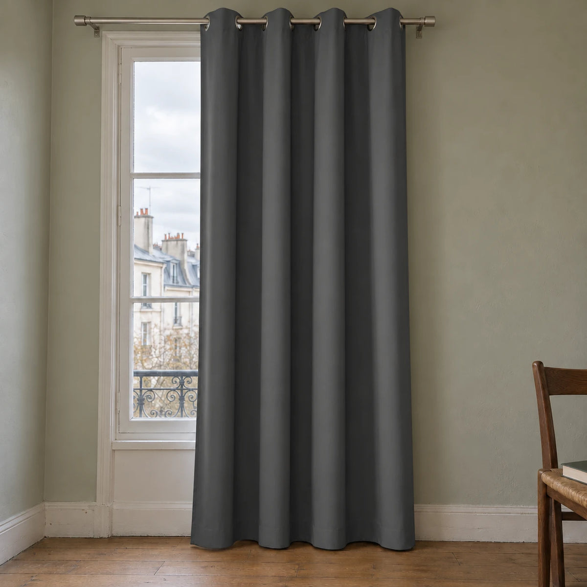Rideau thermique uni gris foncé à œillets, installé devant une fenêtre dans un intérieur aux murs gris vert.